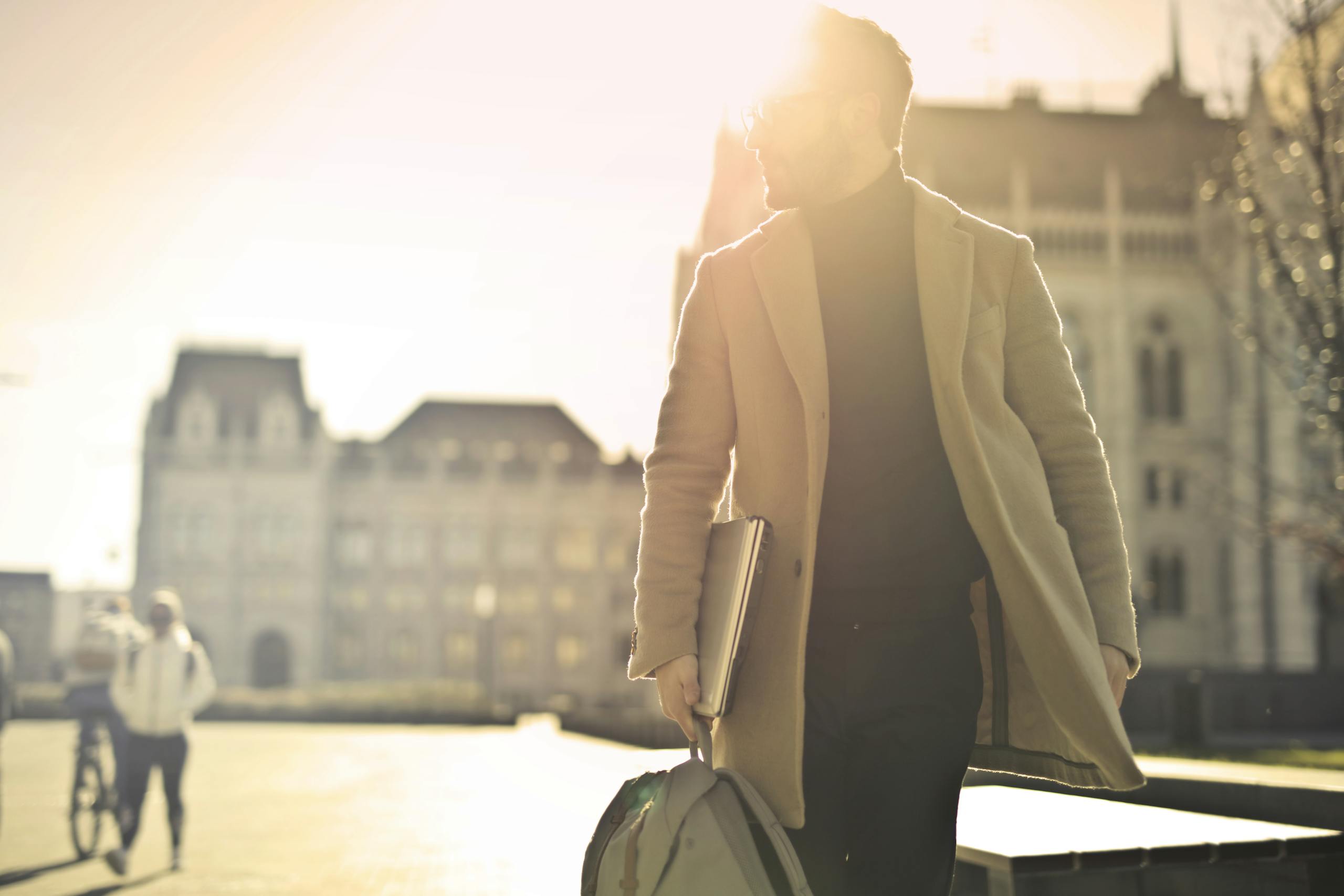 A businessman walks in front of a historic building in Budapest with sun glare illuminating the scene.